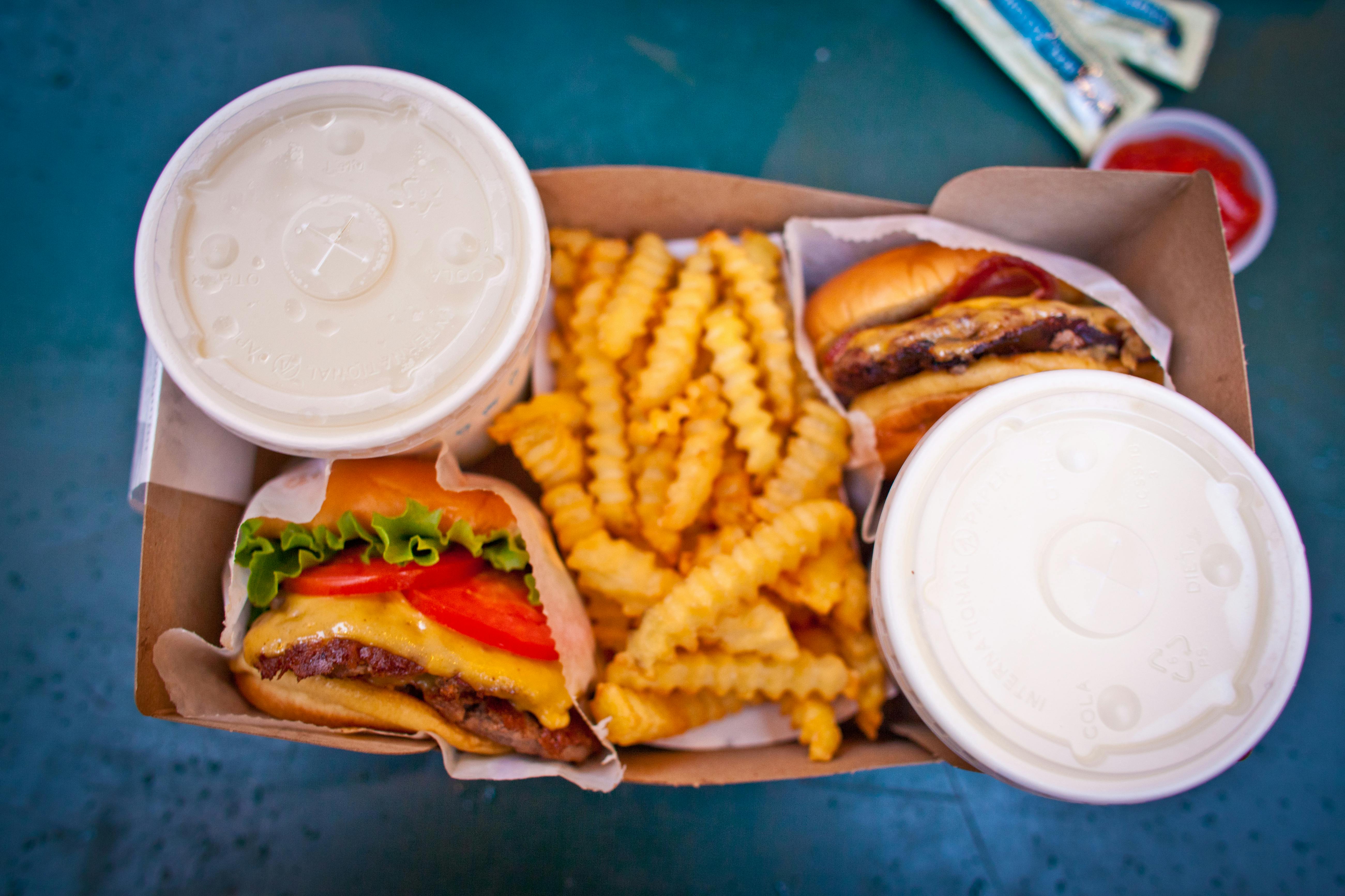 An overview shot of two cheesburgers, French fries, and drinks.